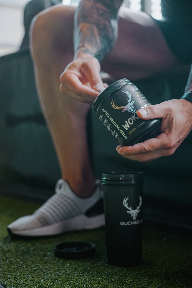 “Athlete scooping Bucked Up Woke AF pre-workout powder into shaker cup before training – high-stimulant pre-workout supplement for energy and focus.”