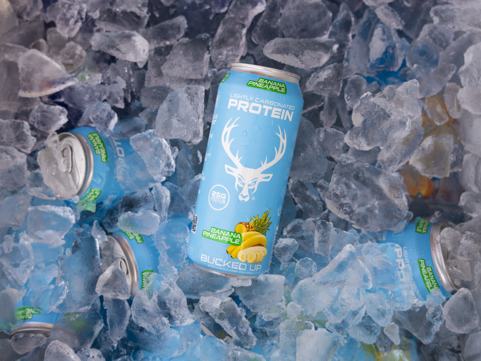 Several cans of lightly carbonated protein drink with a blue label featuring a white deer head logo, pineapple and banana illustrations, and the words 'Bucked Up' are scattered among crushed ice, with one can prominently upright in the center. The cans are partially submerged in the ice, which has a bluish tint, and the background is filled with more ice and cans, creating a cool, refreshing, and energetic atmosphere. The lighting highlights the glossy surface of the cans and the texture of the ice, emphasizing the vibrant colors and branding.